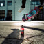 Tabac Wild Ride steht auf Straße. Im Hintergrund springt jemand mit einem Skateboard.